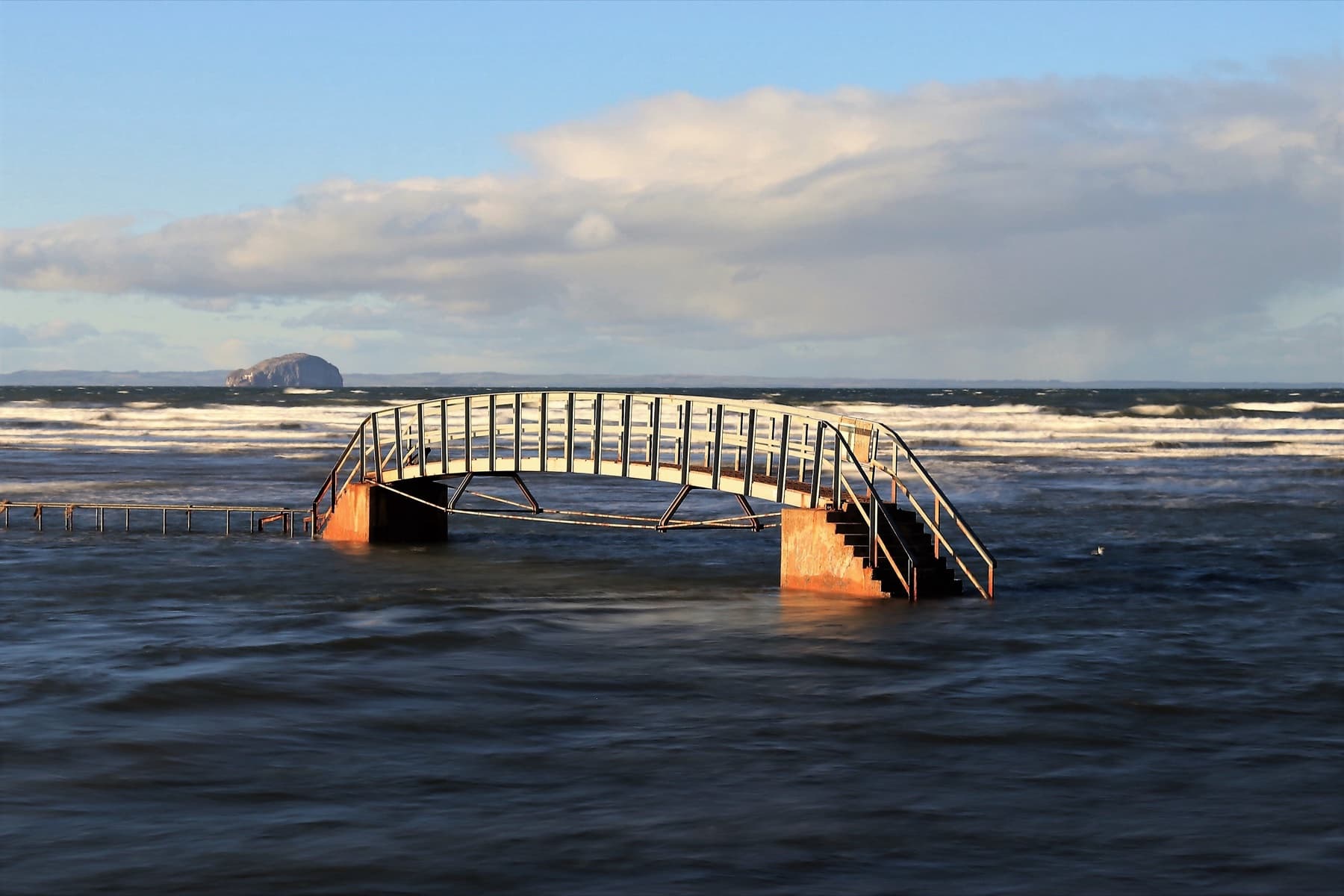 A footbridge over rough coastal water near the Bass Rock